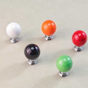 Peut inclure: Cinq boutons de meuble color&eacute;s avec une finition brillante. Les boutons sont blancs, orange, rouges, noirs et verts. Chaque bouton a une forme sph&eacute;rique et une base chrom&eacute;e. Ces boutons d&eacute;coratifs conviennent aux projets de meubles et de d&eacute;coration int&eacute;rieure.