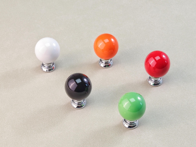 Peut inclure: Cinq boutons de meuble color&eacute;s avec une finition brillante. Les boutons sont blancs, orange, rouges, noirs et verts. Chaque bouton a une forme sph&eacute;rique et une base chrom&eacute;e. Ces boutons d&eacute;coratifs conviennent aux projets de meubles et de d&eacute;coration int&eacute;rieure.