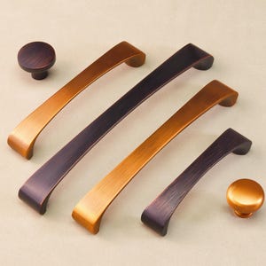 Op de afbeelding: Een assortiment bronzen kastbeslag, waaronder twee knoppen en drie gebogen handgrepen in verschillende maten. Het beslag heeft een geborstelde afwerking en een warme, metallic uitstraling. De opstelling staat op een neutrale achtergrond.