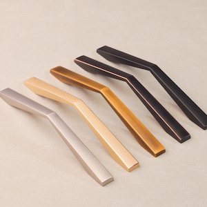 May include: Five cabinet pulls in different finishes: nickel, brass, bronze, copper, and black. The pulls are all the same shape, with a curved, angled design.