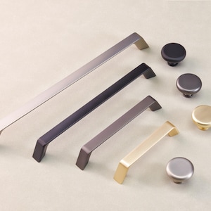 May include: A collection of cabinet hardware, including silver, black, and gold-toned handles and knobs. The handles are rectangular with angled ends. The knobs are round and come in various metallic finishes. These are likely for kitchen or bathroom cabinets.