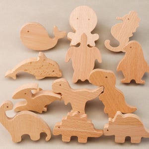 May include: A set of 10 wooden animal puzzle pieces, including a whale, dolphin, octopus, turtle, seahorse, penguin, dinosaur, and three other dinosaurs. The pieces are all natural wood colour and have a smooth finish.