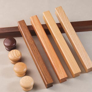 Puede incluir: Cinco tiradores de armario de madera en varios tonos de marrón y madera natural. Los tiradores son rectangulares y tienen un acabado liso y pulido. También hay cuatro pomos de madera en varios tonos de marrón.