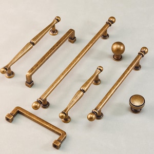 Op de afbeelding: Een assortiment antiek bronzen kastbeslag, inclusief handgrepen en knoppen. De handgrepen variëren in lengte, met afgeronde en vierkante uiteinden. De knoppen zijn bolvormig en schijfvormig, allemaal met een bijpassende afwerking.