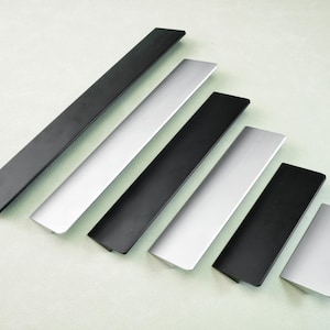 Könnte beinhalten: Sechs moderne Schrankgriffe in verschiedenen Größen, abwechselnd in Mattschwarz und gebürstetem Silber. Die Griffe sind diagonal auf einem hellgrünen Hintergrund angeordnet.