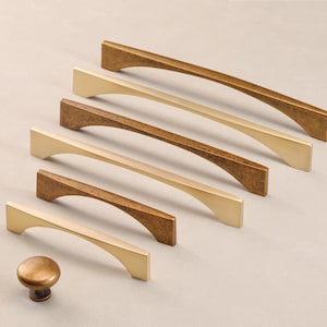 May include: A set of six gold and bronze cabinet pulls with a curved design. The pulls are arranged in a row from largest to smallest. A matching gold knob is also included.