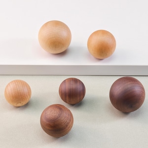 May include: Six wooden spheres, three light brown and three dark brown, arranged on a light brown surface.