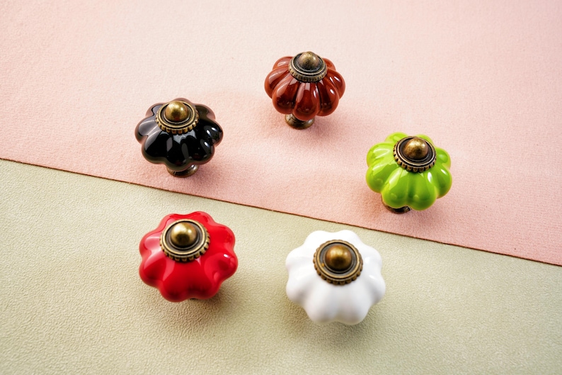 May include: Five decorative cabinet knobs in black, red, white, green, and brown. Each knob has a flower-like shape with a brass-coloured centre and base, suitable for furniture or home d&eacute;cor.