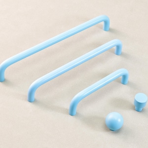 May include: A selection of pale blue cabinet hardware, featuring three bar handles of different lengths, a round knob, and a cylindrical knob. The items are displayed on a neutral surface, highlighting a contemporary design.