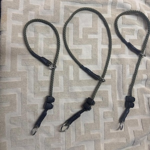 May include: Three green rope dog leads with black accents and metal rings. The leads are arranged in a row on a white fabric background.