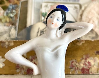 May include: A white porcelain figurine of a woman with a blue and white hat. The figurine is wearing a white dress and has a delicate facial expression.