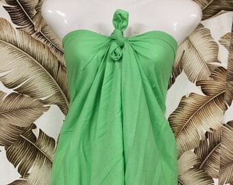 May include: A bright green sarong tied around a white mannequin. The sarong is made of a soft, flowing fabric.
