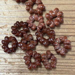 May include: A collection of brown, twisted, ceramic rings. The rings are all the same size and shape, and they are arranged in a random pattern on a wooden surface.
