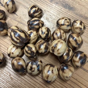 May include: A collection of brown and white patterned beads, likely made from natural materials like bone or wood. The beads are smooth and have a slightly glossy finish.