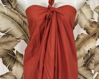 May include: A rust-colored sarong tied around a mannequin. The sarong is made of a soft, flowing fabric and is perfect for a beach day or a casual summer outfit.