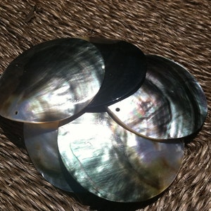 May include: A group of five iridescent black and green mother of pearl shell discs with a hole in the center of each disc. The discs are stacked on top of each other.
