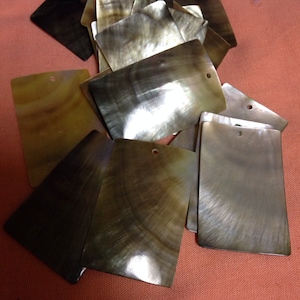 May include: A pile of iridescent, rectangular, mother-of-pearl tiles with a hole in each corner. The tiles are various shades of brown and green.