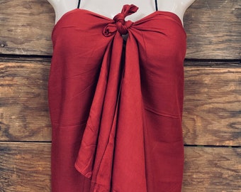 May include: A maroon-colored sarong with a black halter strap. The sarong is tied in a knot at the front and drapes down to the floor.