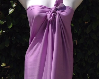 May include: A light purple sarong tied at the bust on a white mannequin. The fabric is draped and knotted, creating a strapless top. The background is a lush green hedge.
