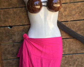May include: A pink sarong tied around a white mannequin torso. The mannequin is wearing a coconut shell bra.