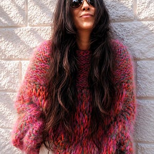 K&ouml;nnte beinhalten: Ein grob gestrickter, &uuml;bergro&szlig;er Pullover mit einer lebendigen, mehrfarbigen Garnmischung aus leuchtendem Pink, Orange und Gr&uuml;n. Das Kleidungsst&uuml;ck hat ein dickes, strukturiertes Gewebe mit flauschiger Optik, langen &Auml;rmeln und einem Rundhalsausschnitt.