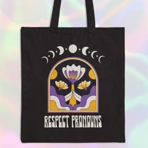 May include: Black tote bag with a graphic of a flower and crescent moons. The text "Respect Pronouns" is printed below the graphic.