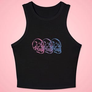 May include: A black sleeveless crop top featuring a graphic print of three skulls arranged in a horizontal row. The skulls are outlined in a gradient of pink, purple, and blue colors, creating a layered effect across the center of the chest.