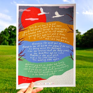 May include: A colorful art print featuring a poem with a red sun, geese, and layered landscape. The text includes the words "Under the Sun" and the author's name, Mary Oliver. The artwork is held by a hand against a green background.