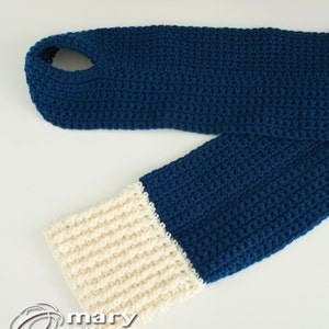 May include: A blue and cream crocheted scarf with a hole at the top. The scarf is made with a simple stitch pattern and has a contrasting cream colored band at the bottom.