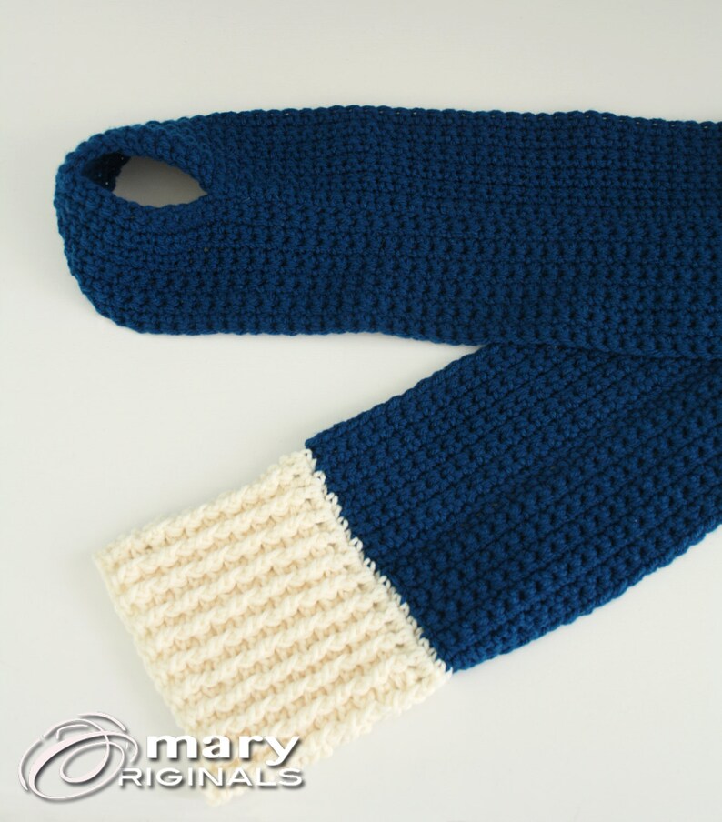 May include: A blue and cream crocheted scarf with a hole at the top. The scarf is made with a simple stitch pattern and has a contrasting cream colored band at the bottom.