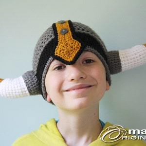 May include: A child wearing a gray, black, and yellow crocheted viking hat with white horns.