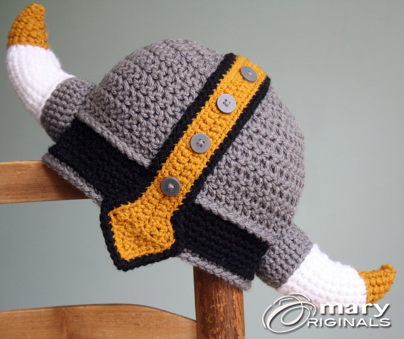 May include: Gray crocheted Viking hat with a yellow and black trim and white horns. The hat has gray buttons on the trim.