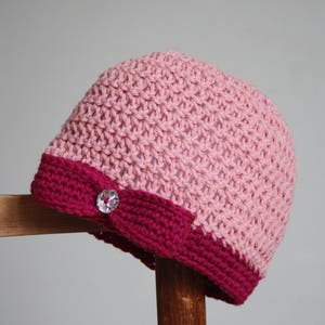 May include: A pink and burgundy crocheted beanie with a sparkly button on the side.