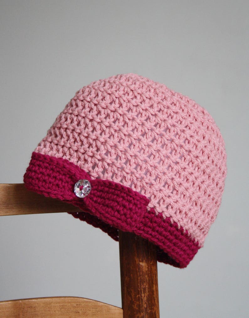 May include: A pink and burgundy crocheted beanie with a sparkly button on the side.