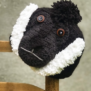 May include: A black and white crocheted monkey head with black button eyes. The monkey head is sitting on a wooden chair.
