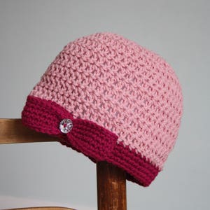 May include: A pink and burgundy crocheted hat with a sparkly button on the side.