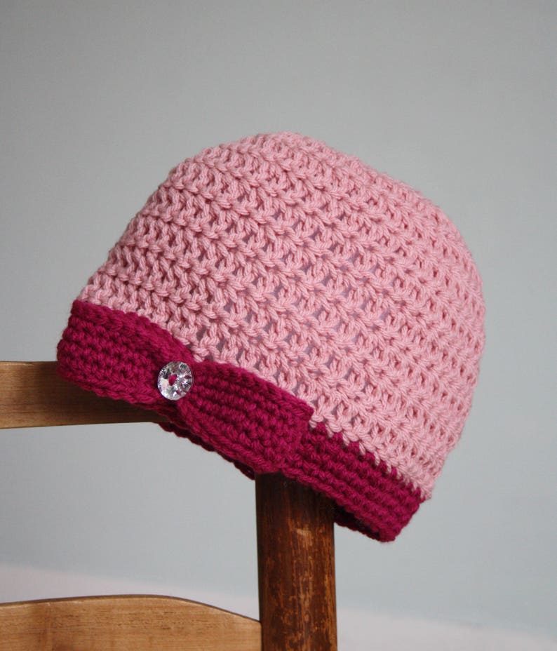 May include: A pink and burgundy crocheted hat with a sparkly button on the side.