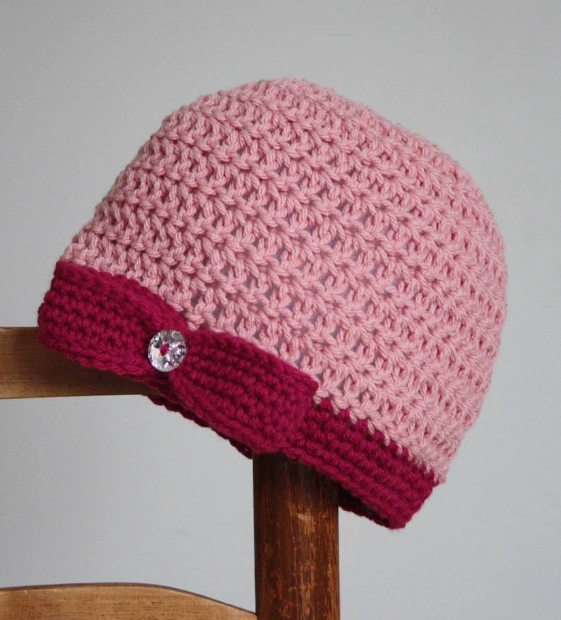 May include: A pink crocheted beanie with a burgundy brim and a sparkly button.
