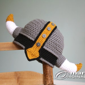 May include: A gray crocheted Viking hat with a yellow and black trim and white horns. The hat has gray buttons on the trim.