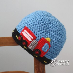 Puede incluir: Un gorro de punto azul con un diseño de camión de bomberos rojo, negro, blanco y amarillo. El gorro tiene un borde negro con una línea amarilla en el centro.