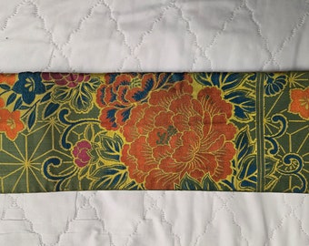 May include: A green fabric with a gold and blue floral pattern. The fabric features large orange flowers with red accents and smaller pink flowers.