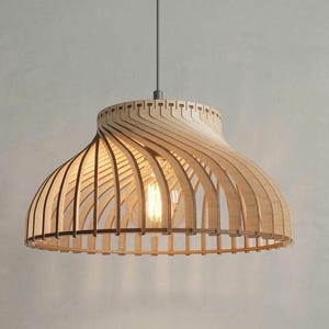 Puede incluir: Lámpara colgante de madera con pantalla en forma de cúpula. La pantalla está construida con listones de madera curvados de color claro, creando un diseño abierto y aireado. Se ve una sola bombilla en el interior. La lámpara cuelga de un cable gris.