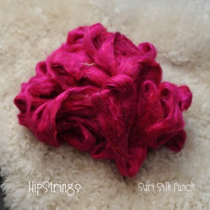 May include: A close-up of a bright pink bundle of sari silk fibres. The fibres are soft and fluffy, and they are perfect for spinning or felting. The text "Sari Silk Punch" is visible in the lower right corner of the image.