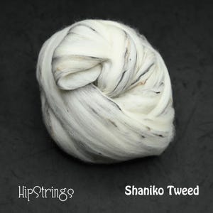 May include: A ball of Shaniko Tweed wool roving. The wool is primarily white with subtle flecks of black and brown throughout. The HipStrings logo and product name are visible.