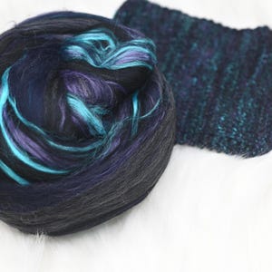 May include: A ball of black, teal, and purple fiber with a sparkly black fabric swatch.