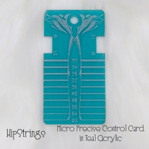 May include: A rectangular teal acrylic tool featuring a central hole at the top, engraved with horizontal lines and numerical markings ranging from 20 to 80, along with side notches labeled 0 and 1/2, designed for precise measurement and control.