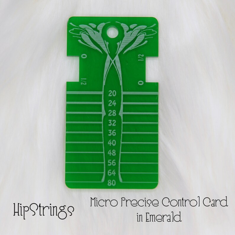 May include: A rectangular green acrylic control card featuring a top hole, decorative etched patterns, and a vertical scale with numerical markings from 20 to 80, alongside side notches labeled 0 and 1/2, with the text HipStrings Micro Precise Control Card in Emerald.