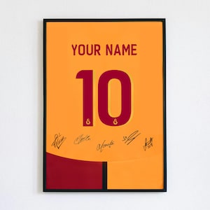 May include: Framed poster featuring a soccer jersey design in orange and maroon. The jersey displays the number 10 in maroon, with the text "YOUR NAME" above. Several signatures are present at the bottom. The background is a solid orange.