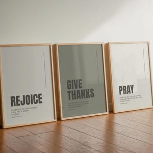 Könnte beinhalten: Drei gerahmte Wandbilder mit hellen Holzrahmen. Das linke Bild ist hellgrau mit dem Text REJOICE und Philippians 4:4. Das mittlere Bild ist olivgrün mit GIVE THANKS und Psalm 107:1. Das rechte Bild ist weiß mit PRAY und Jeremiah 29:12.