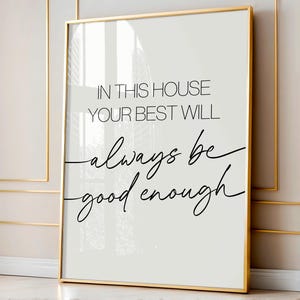May include: A white and grey framed print with the text "In this house your best will always be good enough" in black cursive font.